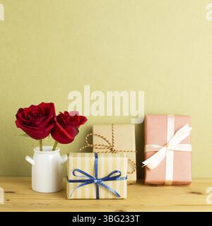 Boîtes-cadeaux avec fleurs roses rouges dans un vase sur une table en bois avec fond kaki. Concept anniversaire, arrangement floral, espace de copie Banque D'Images