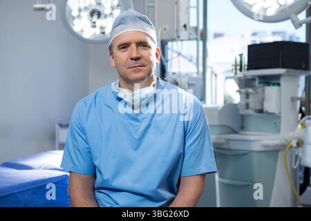 Chirurgien masculin assis dans la salle de chirurgie dans des gommages à côté de la machine d'anesthésie sous les plafonniers Banque D'Images