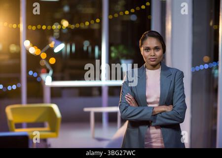 Femme asiatique debout bras croisés portant blazer dans le salon de bureau sous les lumières de la chaîne, espace de copie Banque D'Images