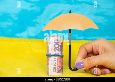 Protection de la hryvnia ukrainienne, la main d'une femme tient un parapluie sur l'argent sur le fond du drapeau ukrainien, l'argent Banque D'Images