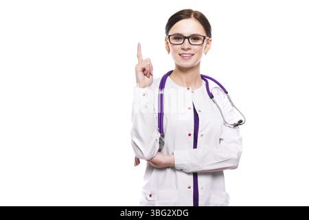 Portrait de jeune femme brune caucasienne attirante souriante médecin debout dans le bureau regardant à la caméra en uniforme blanc avec une zone vide Banque D'Images