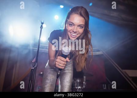 Chanteuse jouant sur scène penchant vers le public tenant un microphone avec lumières et brume Banque D'Images