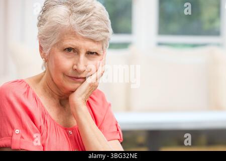 Femme âgée reposant joue sur la main, regardant le spectateur à travers les fenêtres dans le salon, espace de copie Banque D'Images