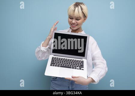 Jeune femme de travail de bureau jolie blonde réussie dans une chemise blanche et jeans démontre un écran d'ordinateur portable avec une maquette pour la publicité. con. d'entreprise Banque D'Images