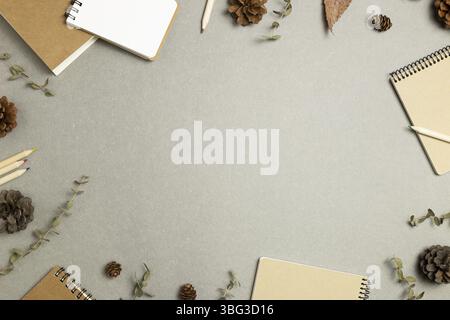 Carnets avec feuilles sèches, cônes en pin sur fond gris. pose à plat, vue de dessus, espace de copie. Lieu de travail et d'étude. Concept automne et hiver Banque D'Images