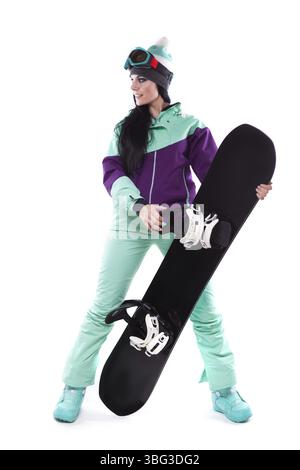 Image verticale, isolée sur blanc, jolie femme caucasienne en tenue de ski violette et pantalon bleu tenant le snowboard noir, jambes écartées, regardez à droite Banque D'Images