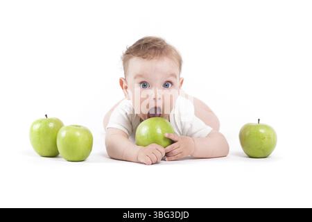 Isolé sur blanc, bébé garçon caucasien en chemise blanche se trouve avec des pommes vertes, bouche ouverte Banque D'Images