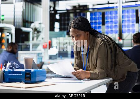 Femme ingénieur principal examinant les données de la ligne de production sur les papiers, gère l'activité de l'usine dans une usine de panneaux solaires pour assurer un contrôle de qualité efficace et un engagement envers la technologie des énergies renouvelables. Banque D'Images