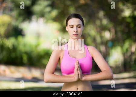 Femme portant un soutien-gorge de sport rose palmiers debout pressés ensemble méditant dans le parc sous la lumière du soleil Banque D'Images