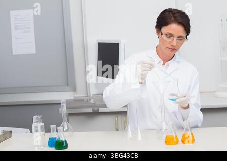 Scientifique femme versant la solution bleue du flacon dans l'entonnoir avec pipette sur la paillasse de laboratoire, copier l'espace Banque D'Images