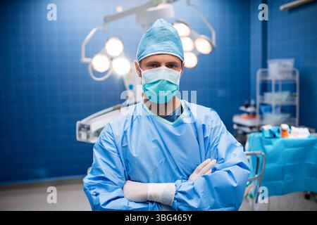 Chirurgien debout sous des lumières chirurgicales à côté d'un chariot en acier inoxydable dans une salle d'opération bleue Banque D'Images