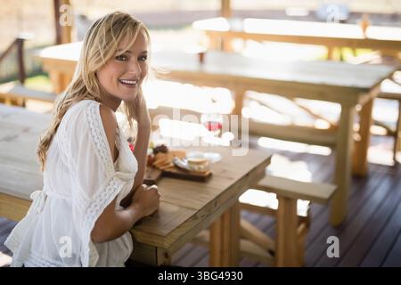 Femme assise à table sur la terrasse sirotant du vin rouge avec planche à fromage et fruits, espace copie Banque D'Images