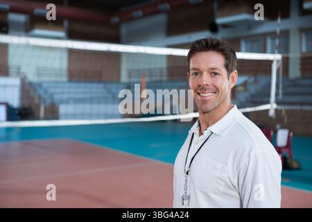 Entraîneur masculin debout près du filet de volley-ball sur le terrain de gymnase tenant le sifflet sur la longe, espace de copie Banque D'Images