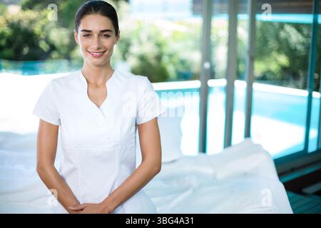 Table de massage reposant sur des draps dans une salle de soins lumineuse avec de grandes fenêtres, donnant sur la piscine bleue Banque D'Images