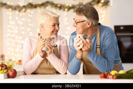 Couple de personnes âgées célébrant la veille de Noël appréciant Cocoa assis dans la cuisine Banque D'Images