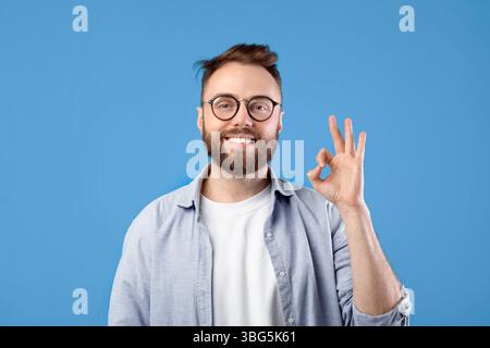 Tout va bien. Portrait d'un homme caucasien heureux montrant un geste OK sur fond bleu de studio Banque D'Images