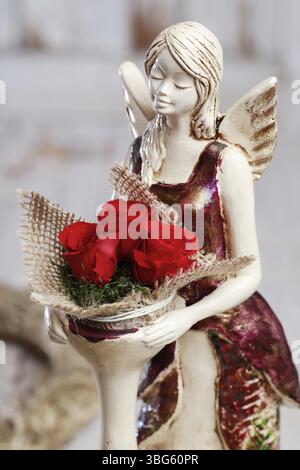 Femme montre comment faire un arrangement floral miniature avec de minuscules roses, de la mousse et un récipient de bougie chauffe-plat. Étape par étape, tutoriel. Un ange tient le f Banque D'Images