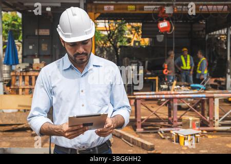 Portrait hispanique ingénieur de construction indien ouvrier masculin sur le chantier de construction avec casque de sécurité regardant l'ordinateur tablette Banque D'Images