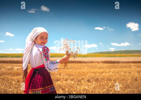 Fille en costume traditionnel de folklore ethnique avec broderie bulgare debout sur un champ de blé doré de récolte Banque D'Images