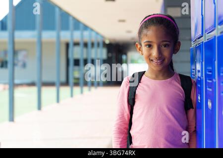 Sac à dos est appuyé contre des casiers en métal bleu dans le couloir extérieur couvert de l'école surplombant l'herbe Banque D'Images
