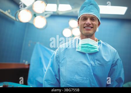 Chirurgien masculin en gommages bleus debout sous les lumières chirurgicales dans la salle d'opération, espace copie Banque D'Images