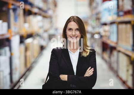 Femme adulte moyenne portant des bras pliants de vêtements d'affaires tout en surveillant l'inventaire de l'entrepôt sur les étagères Banque D'Images