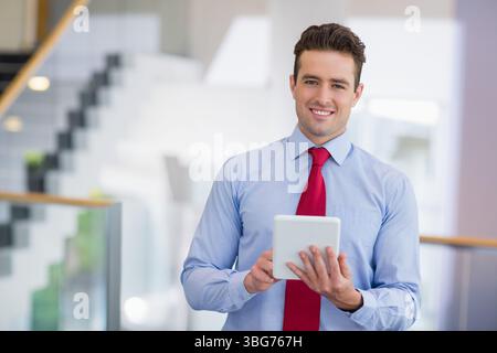 Homme debout dans le hall du bureau tenant une tablette portant une chemise habillée et une cravate près de la balustrade en verre Banque D'Images
