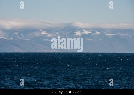 Vue panoramique sur les montagnes enneigées à travers une vaste étendue d'eau bleu profond Banque D'Images