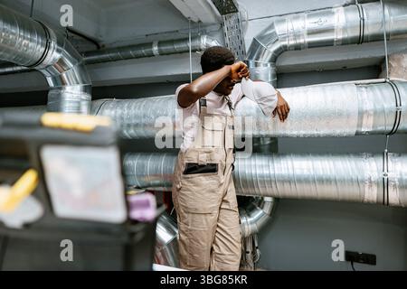 Le travailleur prend une pause à côté des conduits de ventilation dans un milieu industriel pendant l'après-midi Banque D'Images