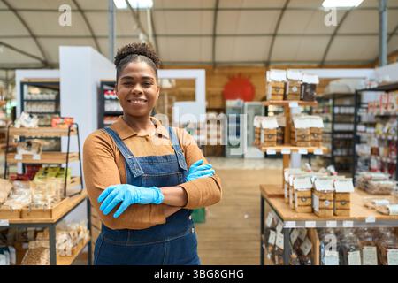 Vendeuse afro-américaine confiante souriante avec les bras croisés dans un magasin zéro déchet Banque D'Images