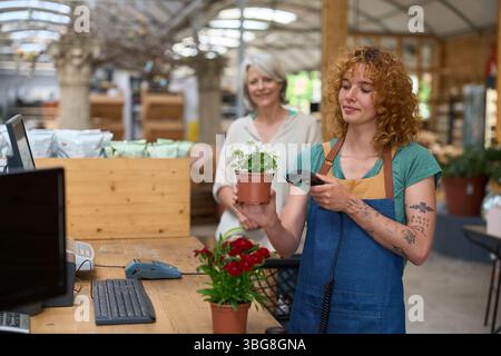 Caissier scannant des fleurs blanches dans le pot à la caisse du centre de jardinage Banque D'Images