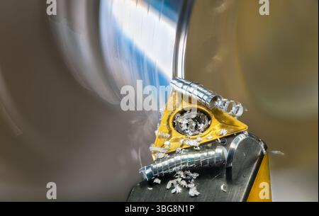 Gros plan sur un foret de tour et sur des copeaux métalliques enroulés en spirale lors de la rotation de la pièce. Fraise à lame tranchante avec plaquette en carbure et copeaux enroulés. Banque D'Images