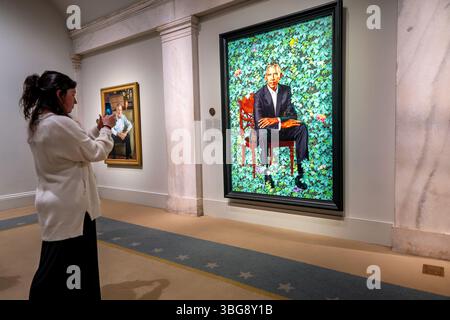 Portrait de Barack Obama par Kehinde Wiley dans la National Portrait Gallery de Washington DC | WASHINGTON D.C., États-Unis — Un visiteur du musée capture le portrait de Barack Obama de Kehinde Wiley en 2018 sur un smartphone à la National Portrait Gallery, avec un portrait de George W. Bush visible sur le mur adjacent. La collection présidentielle de la galerie, le seul ensemble complet à l'extérieur de la Maison Blanche, est logée dans l'ancien bâtiment du Bureau des brevets, un monument de la Renaissance grecque achevé par étapes entre 1836 et 1867. Banque D'Images