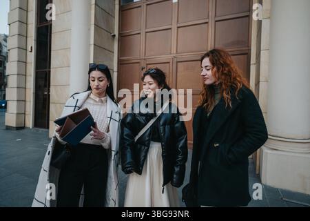Trois femmes discutent et examinent des articles à l'extérieur près d'un grand bâtiment Banque D'Images