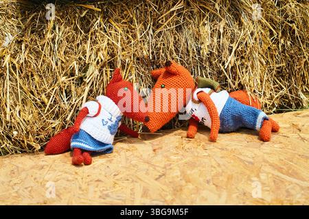 Deux jouets de renard en tricot doux avec des vêtements assis par une botte de foin, créant une scène de campagne confortable avec des éléments faits à la main Banque D'Images