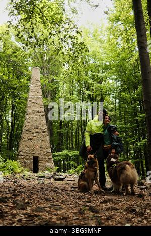 Couple randonnée avec deux chiens - berger allemand et australien à un monument en pierre dans les bois de la montagne Vujan, Serbie. Un moment romantique et actif Banque D'Images