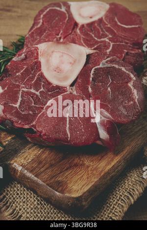 Knuckle sur l'os, viande crue pour ossobuco, sur une planche à découper en bois, avec un brin de romarin, et des épices, vue de dessus, pas de gens Banque D'Images