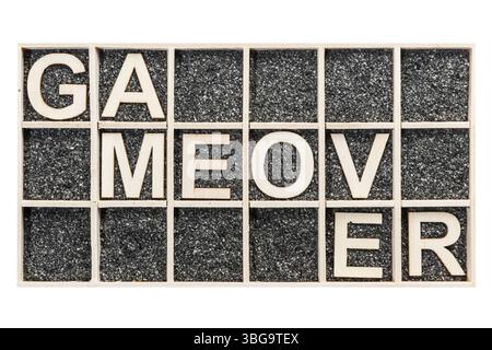 Lettres en contreplaqué disposées dans une boîte de collecte avec du sable décoratif noir représentant le mot cassé GAME OVER dans la vue de dessus sur fond blanc Banque D'Images