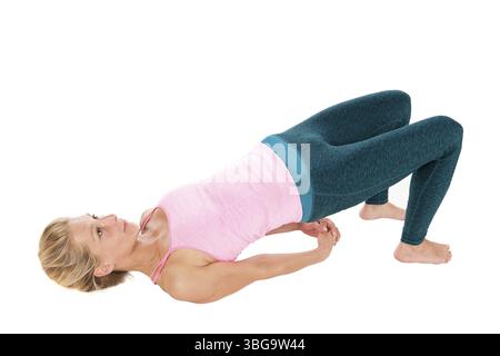 Vue surélevée de profil de corps entier d'une femme blonde d'âge moyen dans le yoga pose le pont (Sethu Bandhasana) avec les bras reposant à nouveau sur le sol Banque D'Images