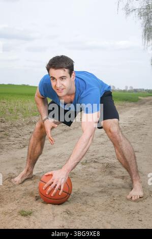 Photo frontale grand angle d'un jeune homme portant un T-shirt bleu, un short de sport noir court et pieds nus dans une posture accroupie penchée vers l'avant, une main au repos Banque D'Images