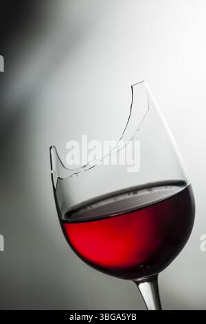 Plan studio du haut d'un verre à vin brisé rempli de vin rouge devant un fond texturé avec dégradé clair et foncé Banque D'Images