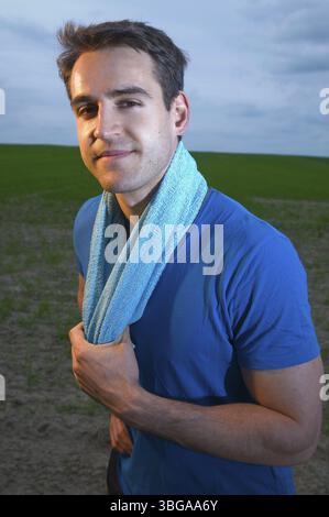 Photo latérale tête et épaules d'un jeune homme portant un T-shirt bleu et une serviette bleue autour du cou regardant dans la caméra Banque D'Images