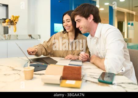 Couple concevant l'intérieur de la maison avec conseiller en utilisant un ordinateur portable dans la salle d'exposition de meubles Banque D'Images