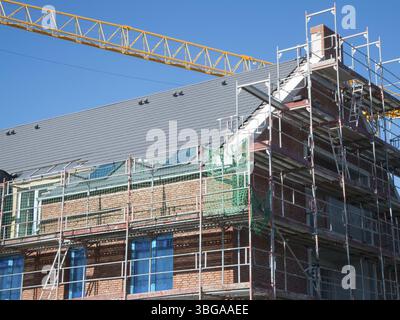 Vue partielle de l'échafaudage sur un bâtiment de plusieurs étages nouvellement construit avec revêtement en briques et flèche de grue jaune contre un ciel bleu Banque D'Images
