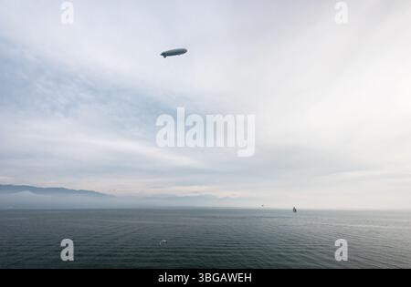 Zeppelin survole la mer. Image grand angle d'un dirigeable gris planant au-dessus du lac Bodensee, surface de l'eau partiellement couverte de brouillard, jour clément. Banque D'Images