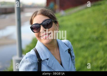 Portrait en gros plan d'une femme souriante portant des lunettes de soleil lors d'une promenade – joyeux mode de vie en plein air Banque D'Images