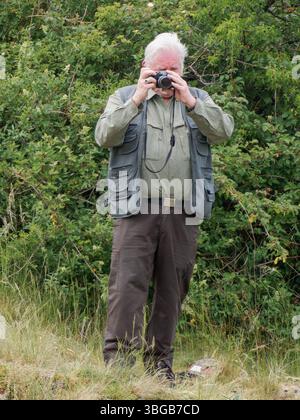 Homme âgé photographiant la nature avec un appareil photo dans un paysage de campagne, Yonne, France. Banque D'Images