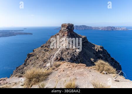 Vue à travers l'arc de pierre encadrant le sentier Skaros Rock et les ruines avec des randonneurs et la caldeira en toile de fond à Santorin Grèce sous un ciel bleu vif. Banque D'Images