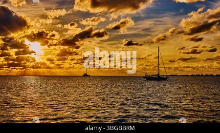 Coucher de soleil doré sur la mer dans les îles Abacos des Bahamas avec des voiliers en arrière-plan. Banque D'Images