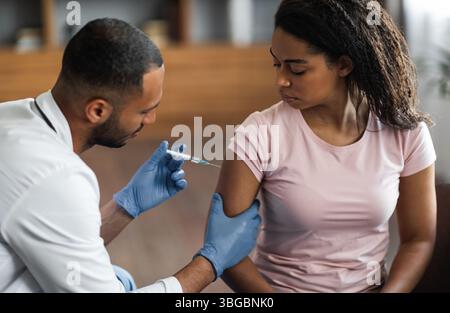 Beau homme noir faisant l'injection dans l'épaule pour la patiente Banque D'Images